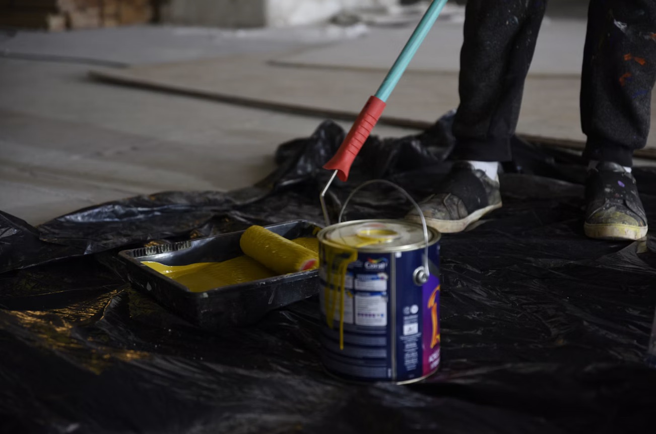 Målarroller, färgtråg och färgburk på täckplast