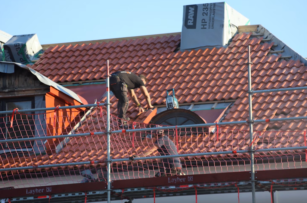 Takläggare lägger tegel på ett tak bakom byggnadsställning